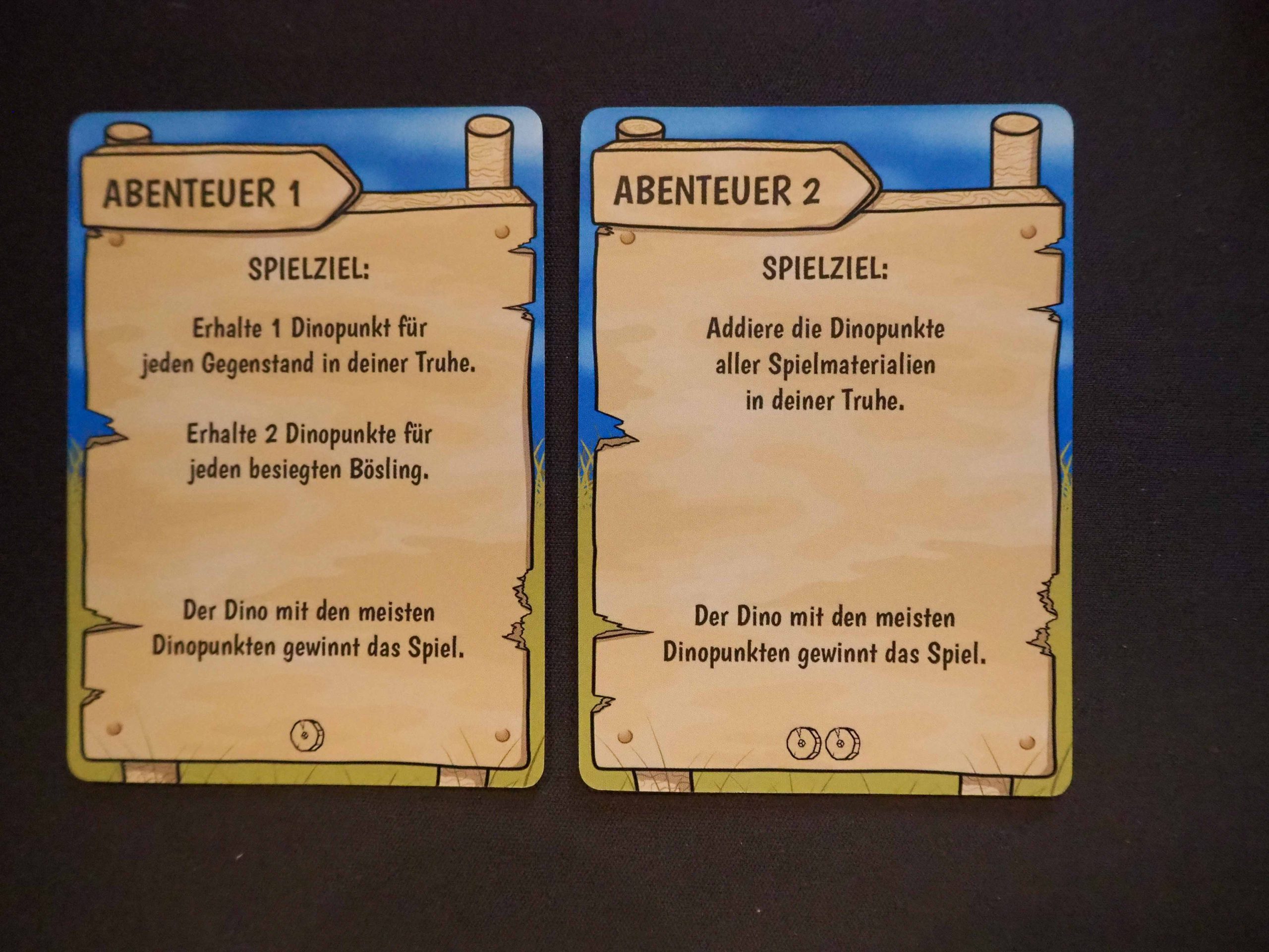 Zwei Abenteuerkarten auf schwarzem Tisch nebeneinander.