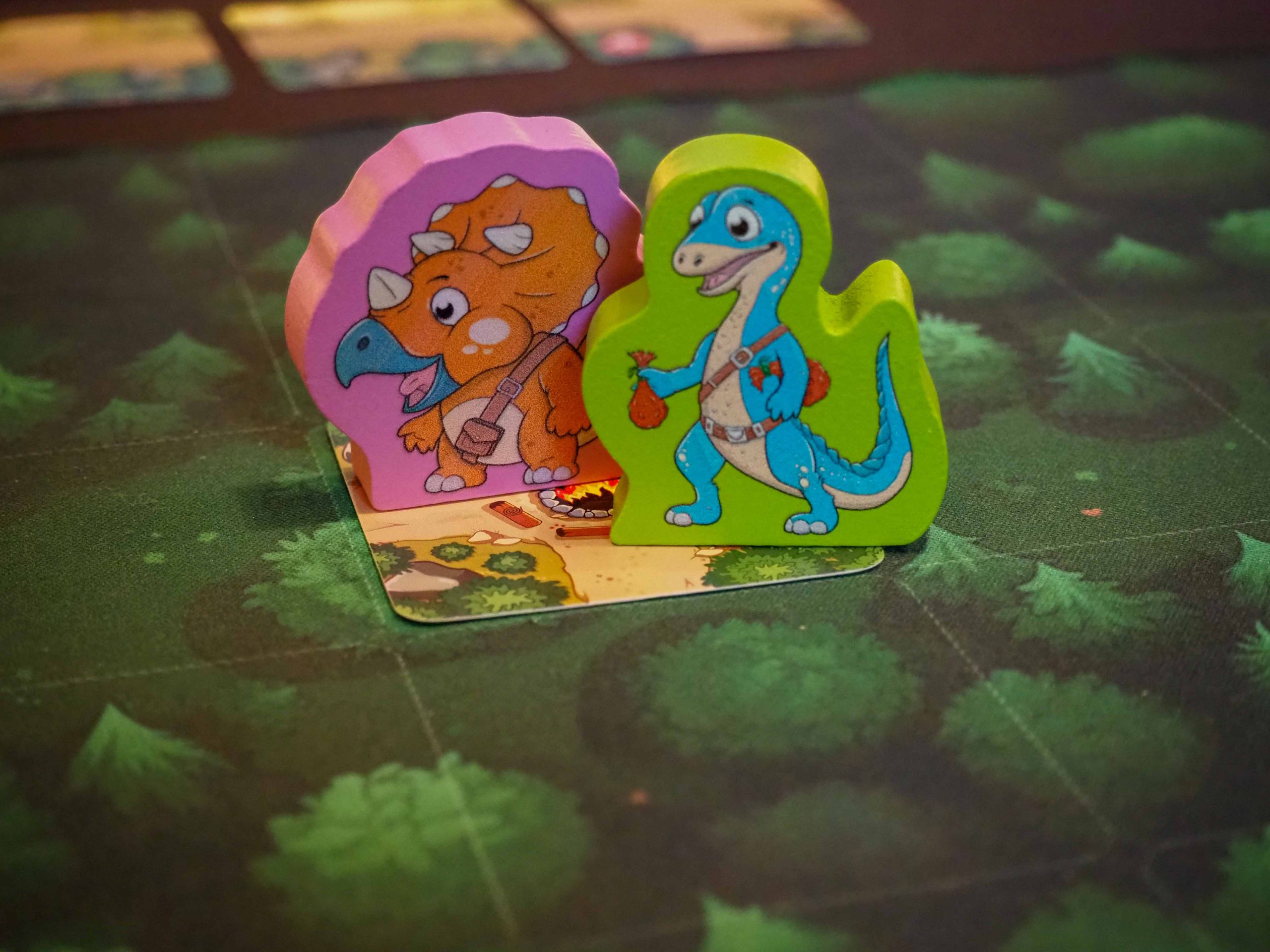 Zwei Dino Holzfiguren stehend auf grünem Untergrund. Eine Figur ist grün und eine rosa.