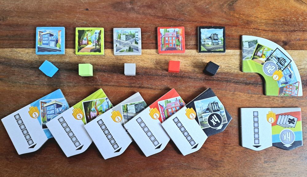 Zu sehen sind die fünf verschiedenen Gebäudeplättchen samt Spielsteinen und die Wertungsplättchen.