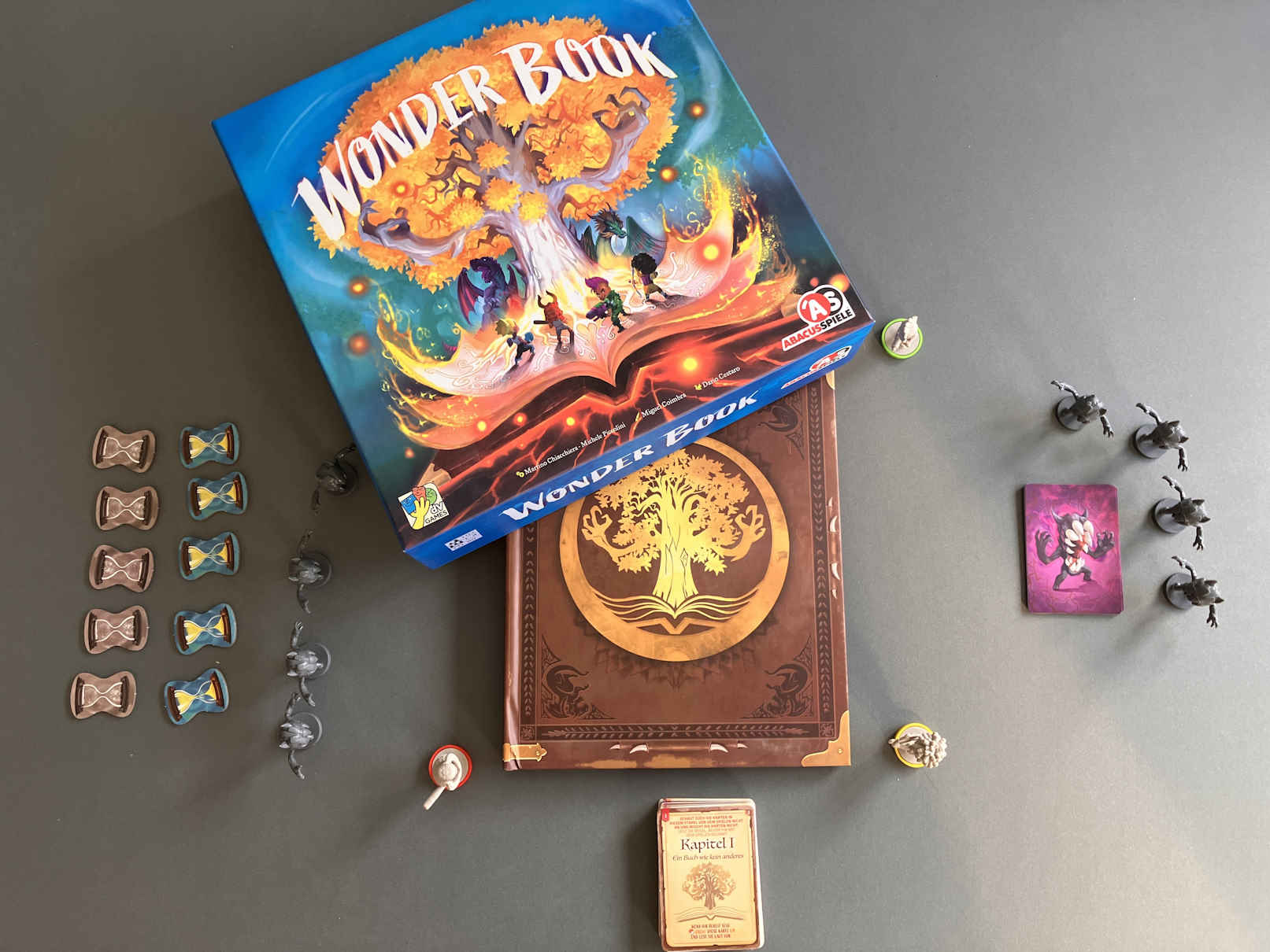 Spielstart - das geschlossene Buch liegt auf dem Tisch, drumherum stehen die Spielfiguren.