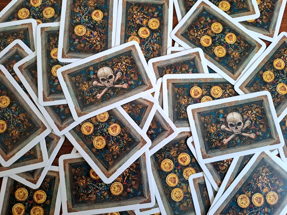 Zu sehen ist ein wildes Durcheinander von Schatzkarten mit den Werten 2-6. Obenauf liegen die beiden Fluchkarten.