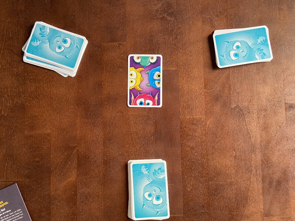 Drei verdeckte Kartenstapel, eine Karte aufgedeckt in der Tischmitte