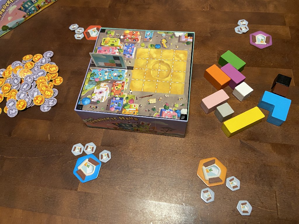 Die Schachtel mit Spielbrett steht in der Mitte des Tisches, drum herum liegen die Marker der Spielenden.