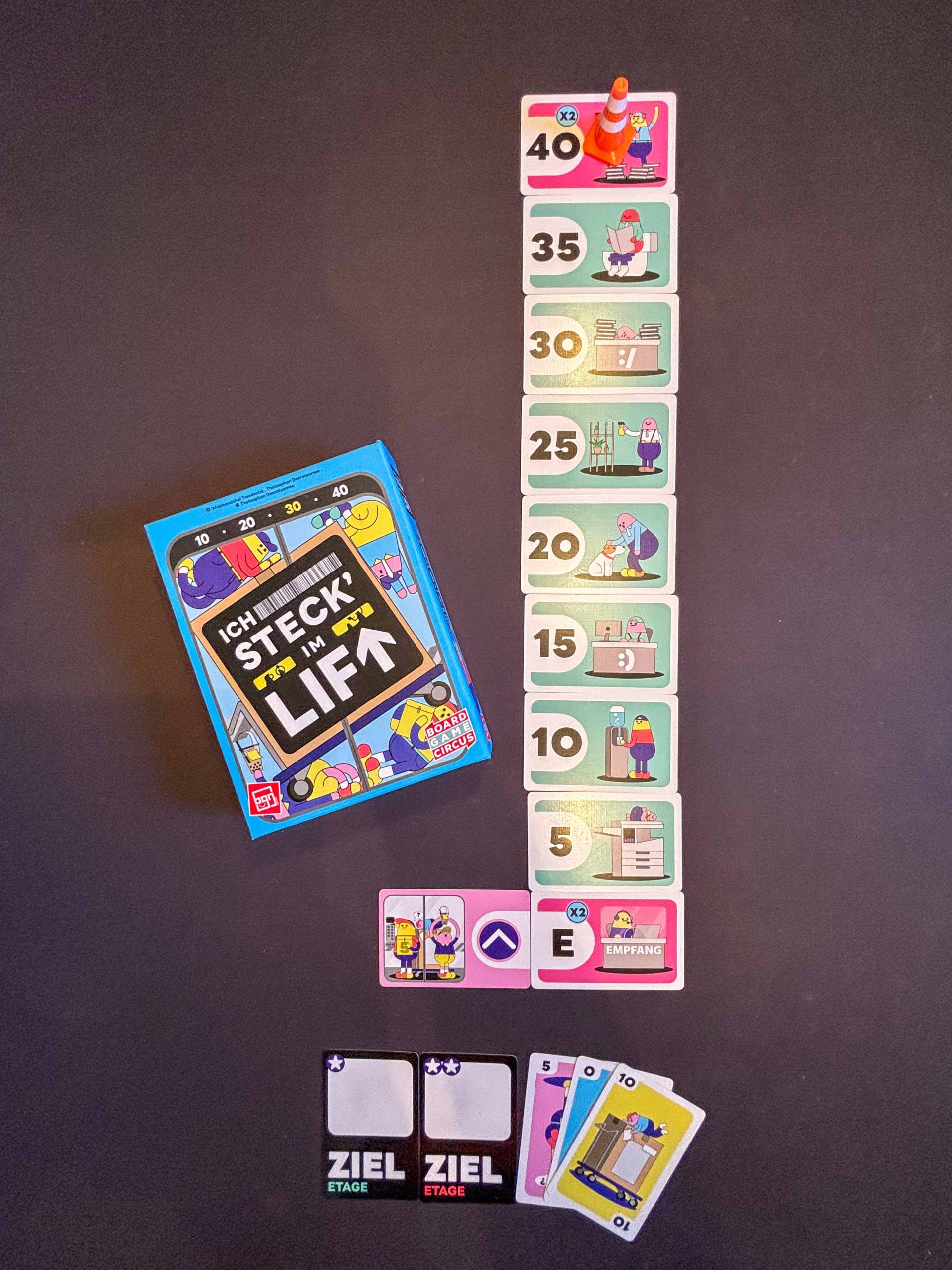 Karten die Stockwerke symbolisieren liegen übereinander auf schwarzem Hintergrund. Spielschachtel links schräg im Bild.