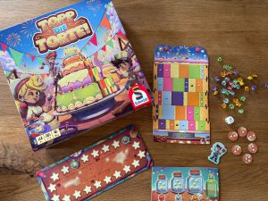 Auf dem Bild ist die Spielschachtel des Spiels sowie einige Materialien aus der Schachtel zu sehen.