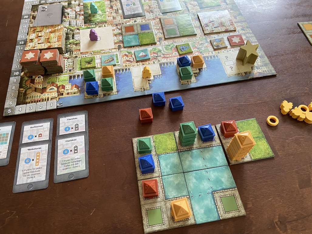 Spielsituation. Vier Geländeplättchen wurden angebaut, darauf Gebäudeteile, daneben erhaltenevAuftragskarten