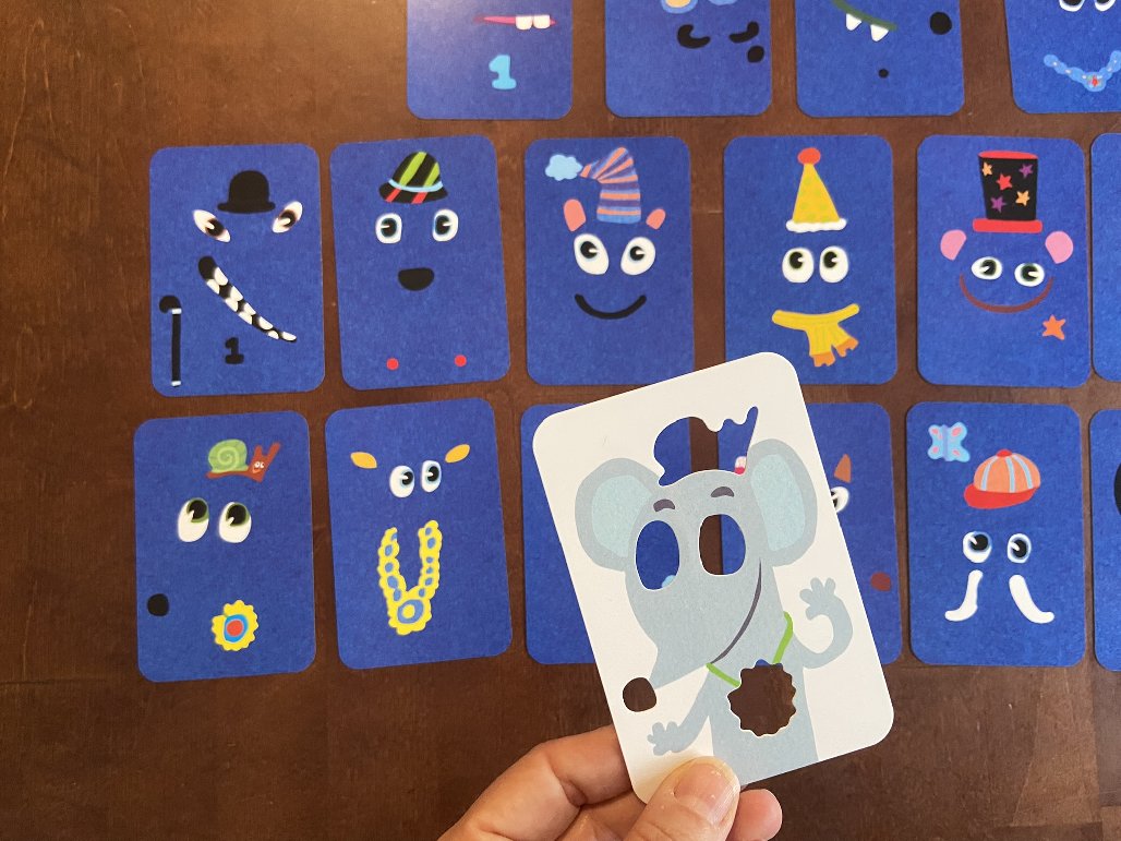 Eine Schablone mit fehlenden Gesichtsteilen über den ausgelegten Karten