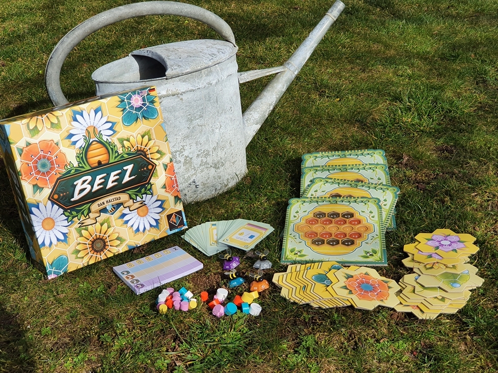 Spielkarton und Inhalt auf Wiese ausgebreitet. Eine Giesskanne im Hintergrund