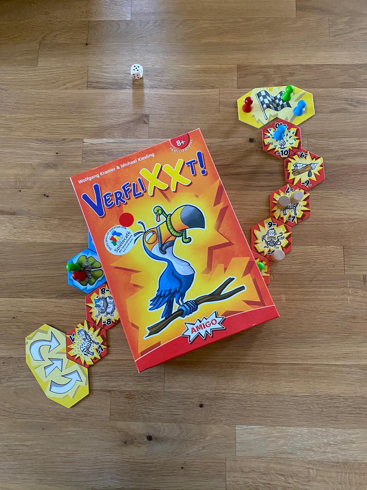 Zu sehen ist das Spielmaterial von Verflixxt sowie die Verpackung