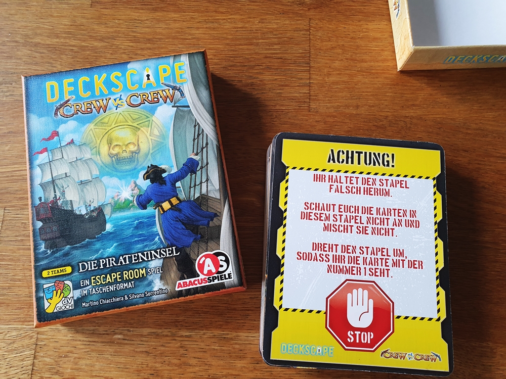 Spieldeckel und Kartenstapel. Gezeigt ist die Unterseite mit der Anweisung, den Kartenstapel umzudrehen