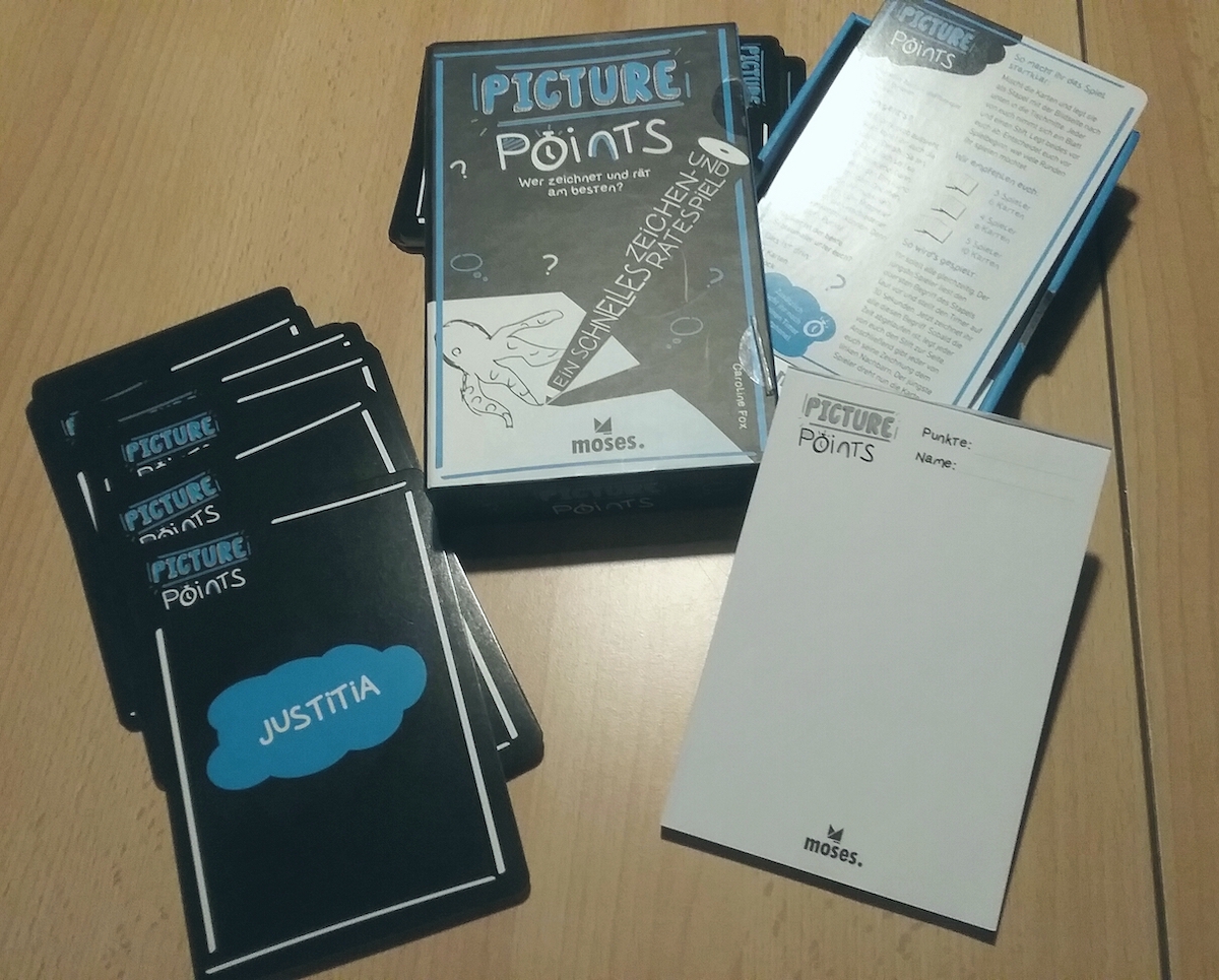 Die Spielpackung mit dem Inhalt, bestehend aus einem weißen Block und Karten mit Begriffen, liegt auf dem Tisch.