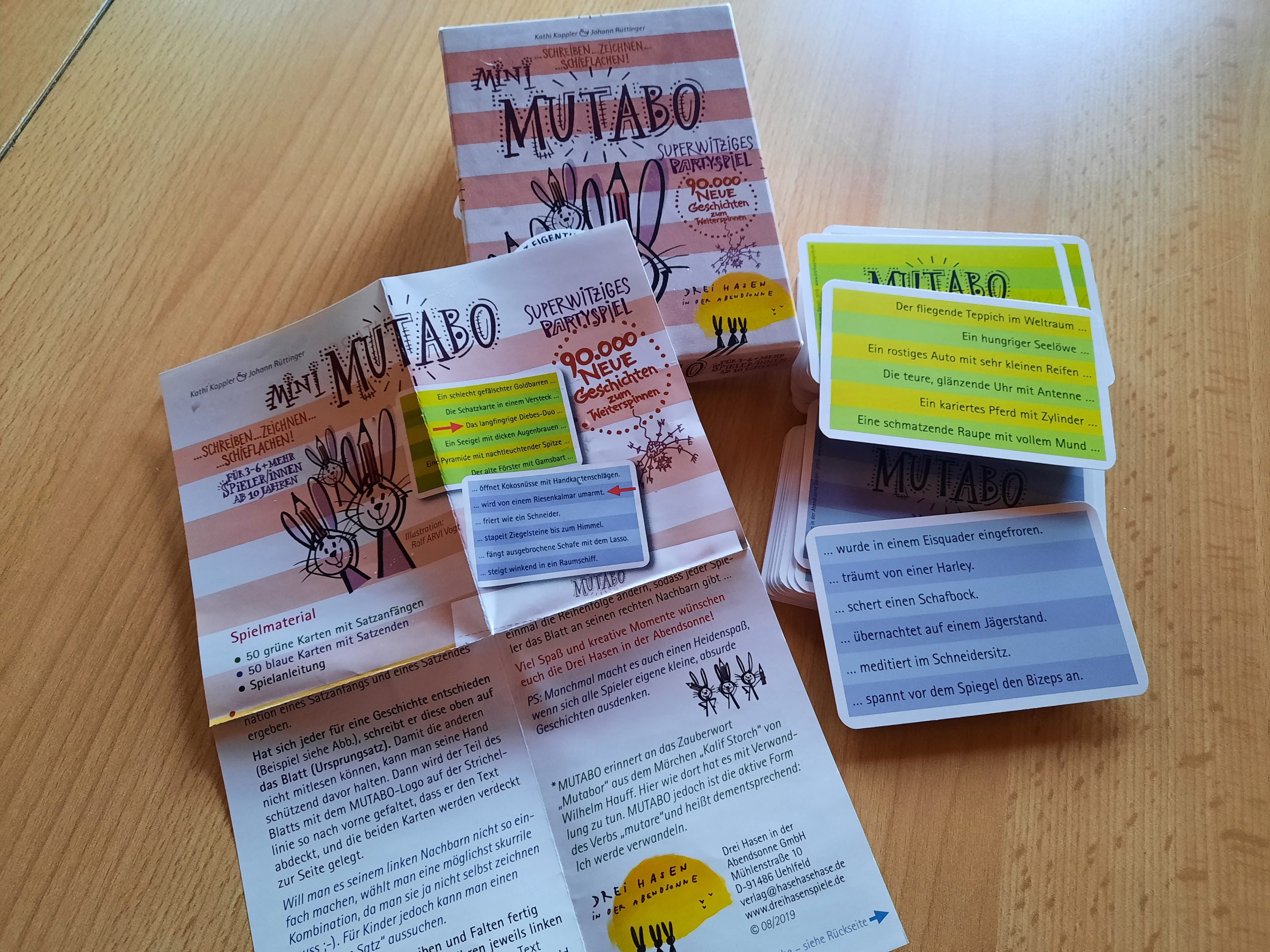 Die Spieleverpackung, die Anleitung und zwei Kartenstapel mit grünen und blauen Karten liegt auf dem Tisch.