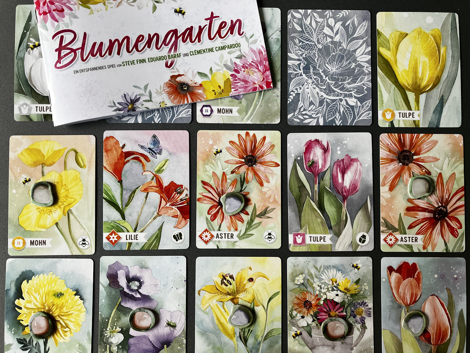 3 Kartenreihen der Blumenkarten liegen offen auf dem Tisch, darüber die Spielanleitung
