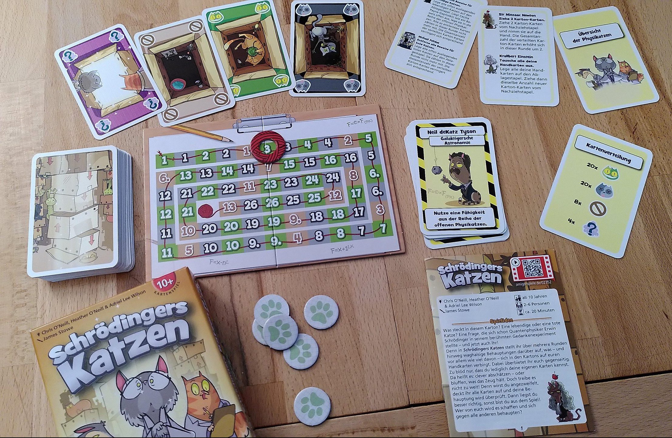 Überblick über das Spielmaterial, Karten mit lebenden Katzen, toten Katzen, leeren Kartons und der Heisenbergschen Unschärferelation, eine Tafel für die Ansagen und Physikatzen-Karten.