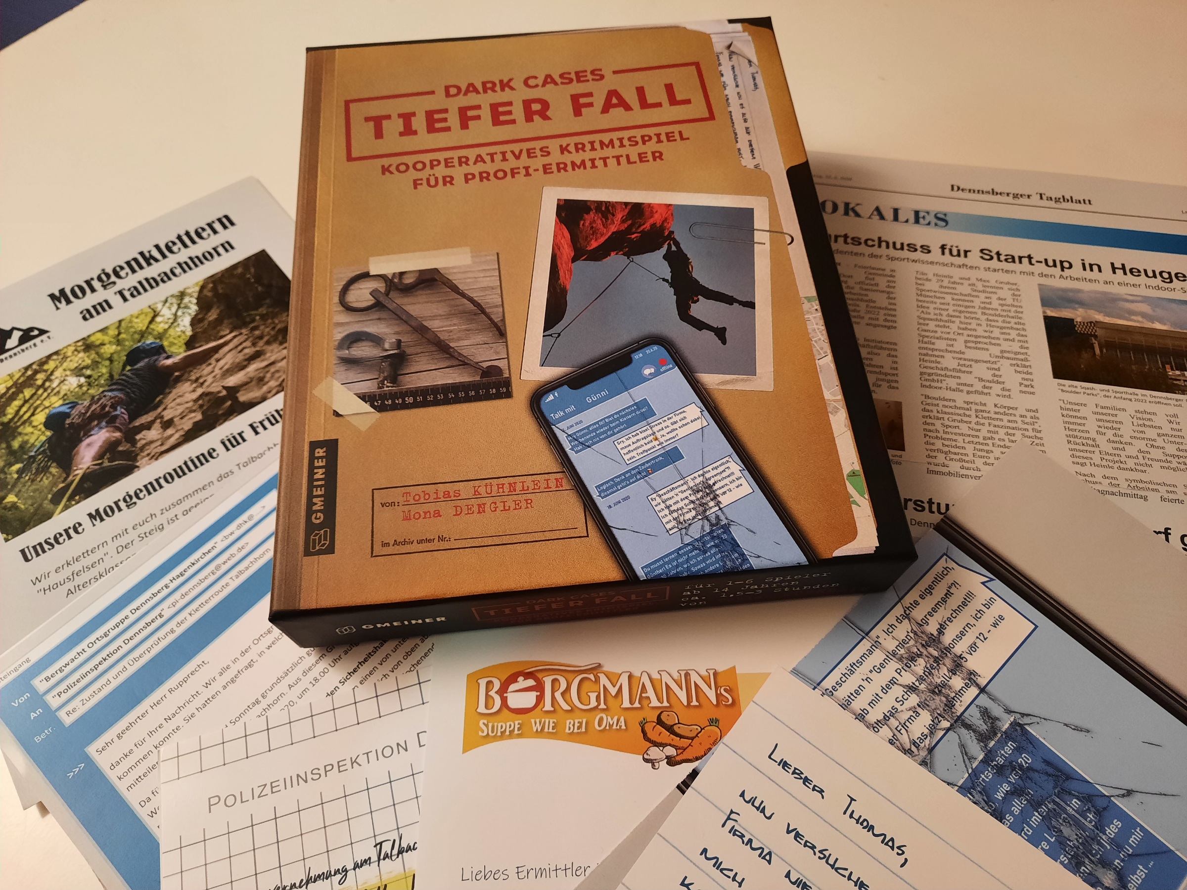 Die Spielepackung und mehrere Blätter mit Infomaterial, als Inhalt des Spiels, liegen auf dem Tisch