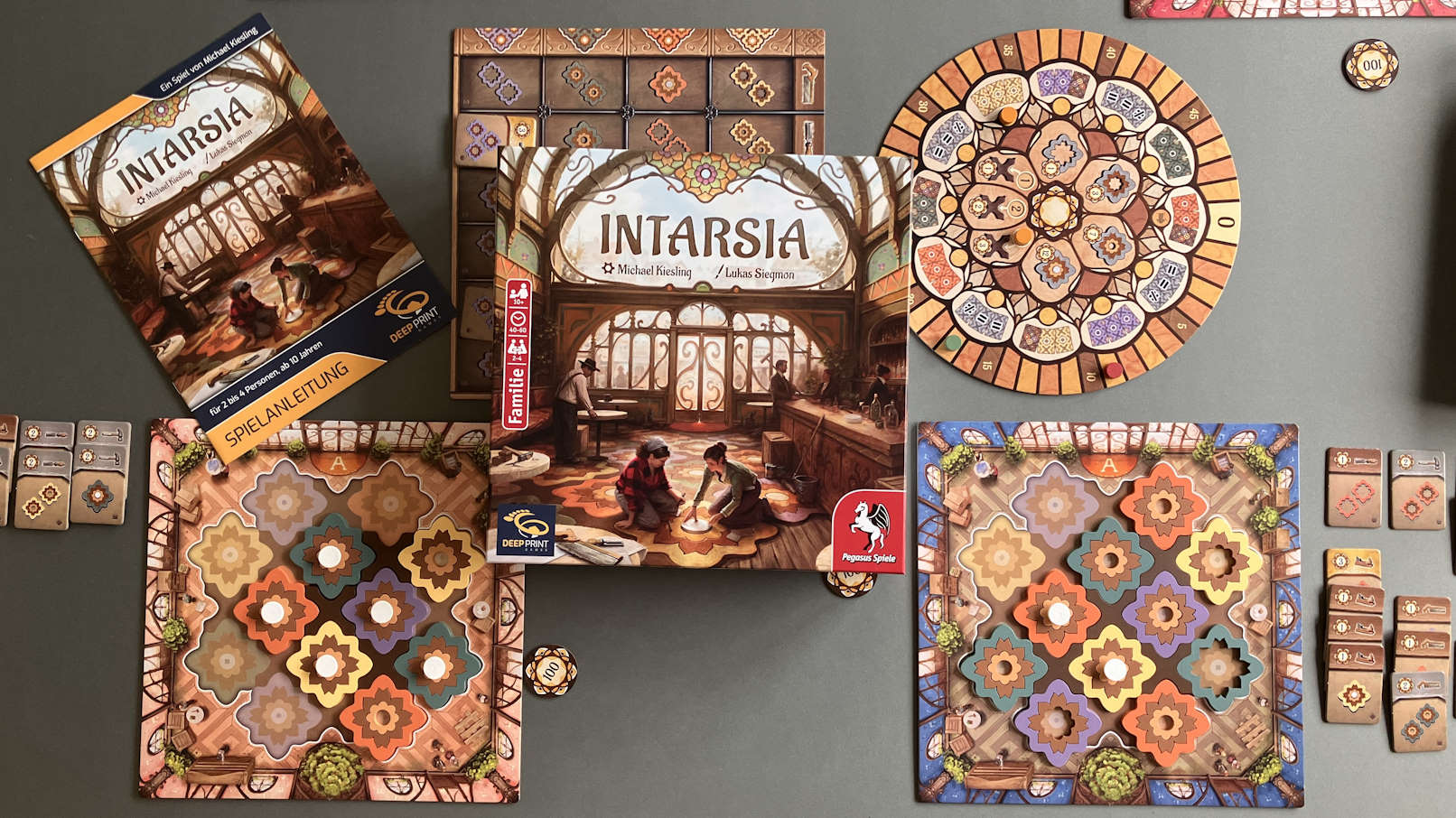 Für ein 4 Personenspiel ausgebreitetes Spiel. Die Spielertableaus, die Spielschachtel im Bild.