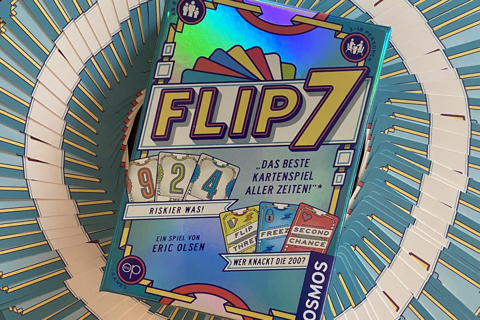 Die Schachtel des Spiels Flip 7 auf einem Ring aus Karten.