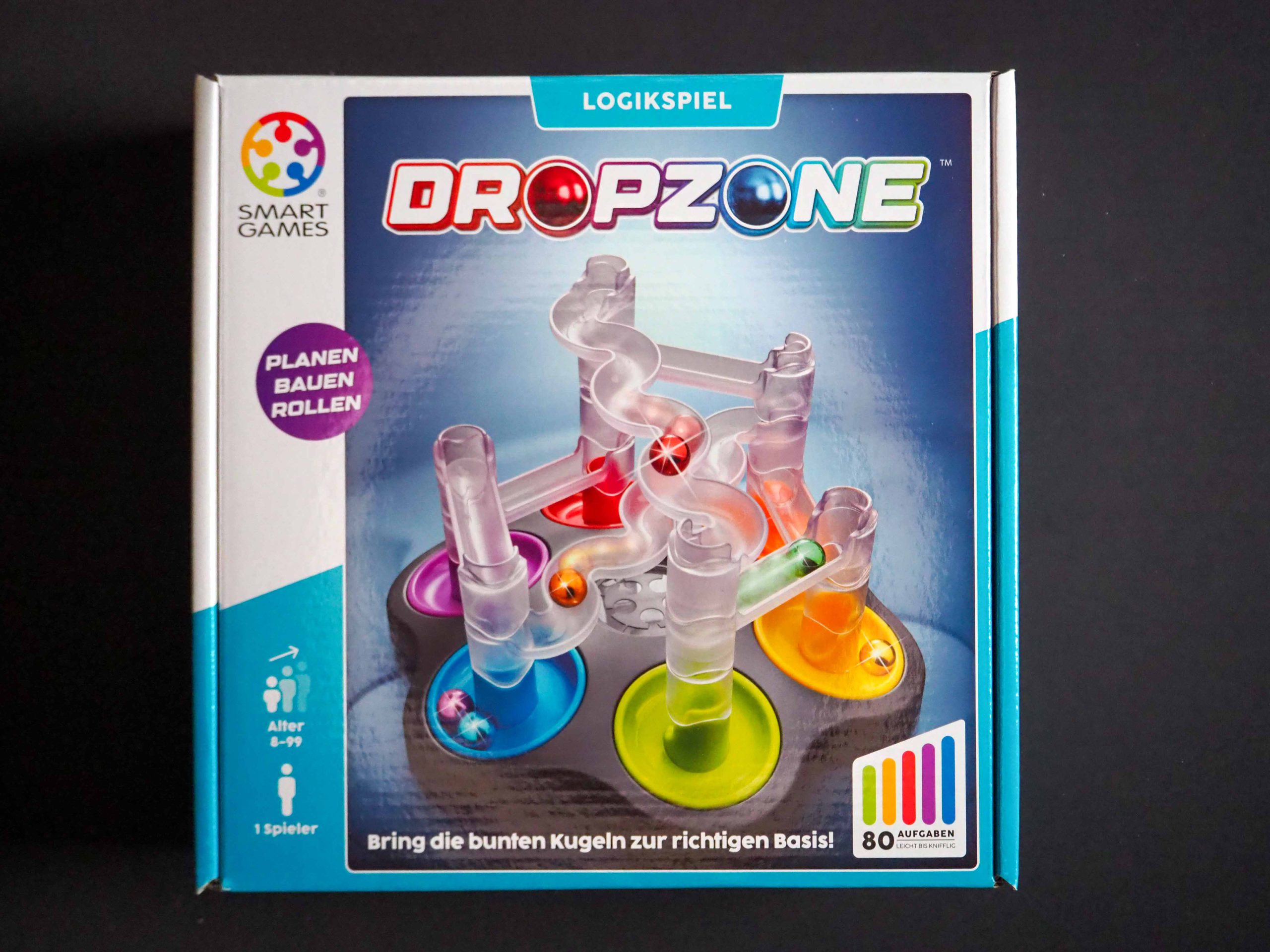 Spielschachtel von DropZone, Hauptfarben in blau, mittig eine Kugelbahn und links oben das Logo von Smart Games