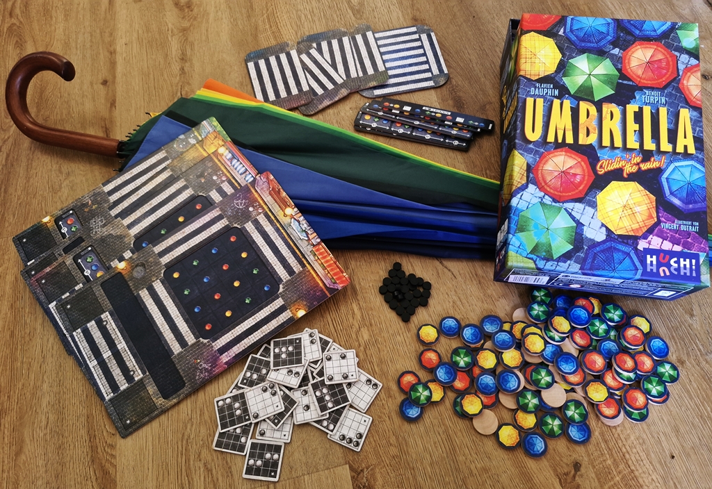 Spielkarton und Inhalt, darunter ein bunter Regenschirm